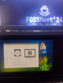 Laptop showing the installation screen of an IT@School GNU/Linux distribution, with the FOSSMeet'24 stage in the background.
